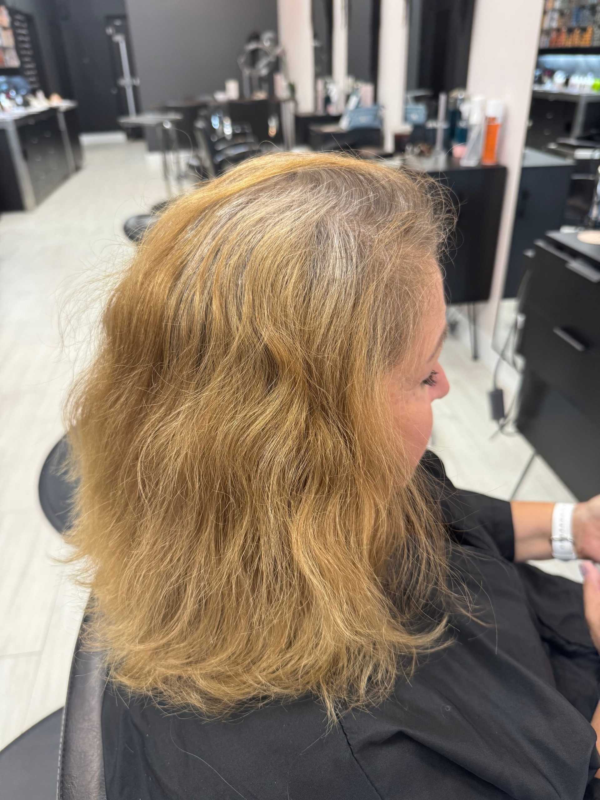 Woman in salon chair with medium-length, wavy blonde hair, hair products in background.